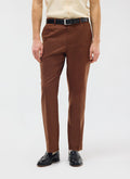 A model wears the Percival Tailored Linen Trousers in brown, styled with a black belt and loafers.