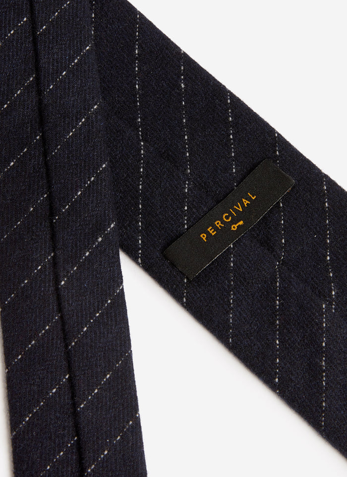 A close-up of the navy Textured Stripe Tie from Percival, showing the subtle pinstripe detail and the woven brand label.