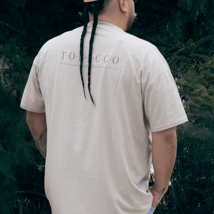 Person wearing Tobacco Medicine Tee in beige Indigenous streetwear graphic shirt back view
