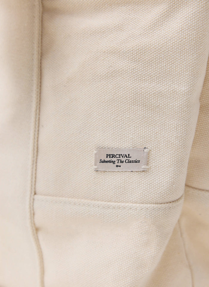 A close-up of the woven 'Subverting The Classics' label on the ecru cotton canvas tote bag from Percival.
