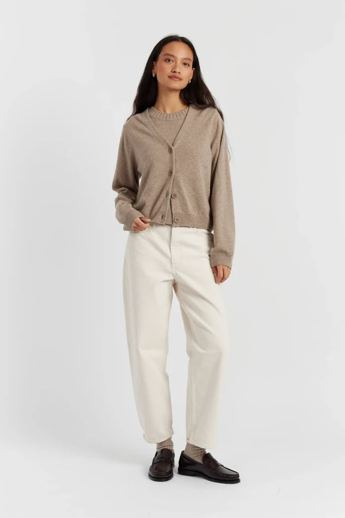 Woman wearing a beige cardigan, white pants, and dark shoes on a white background