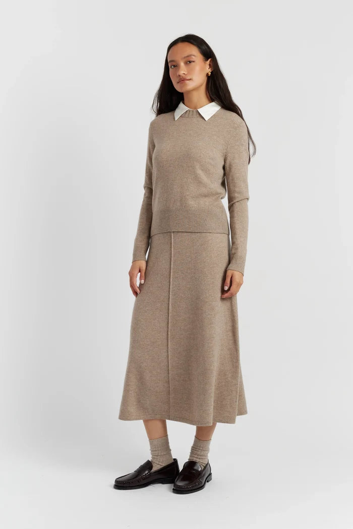 Woman wearing a beige sweater dress with a white collar on a light gray background