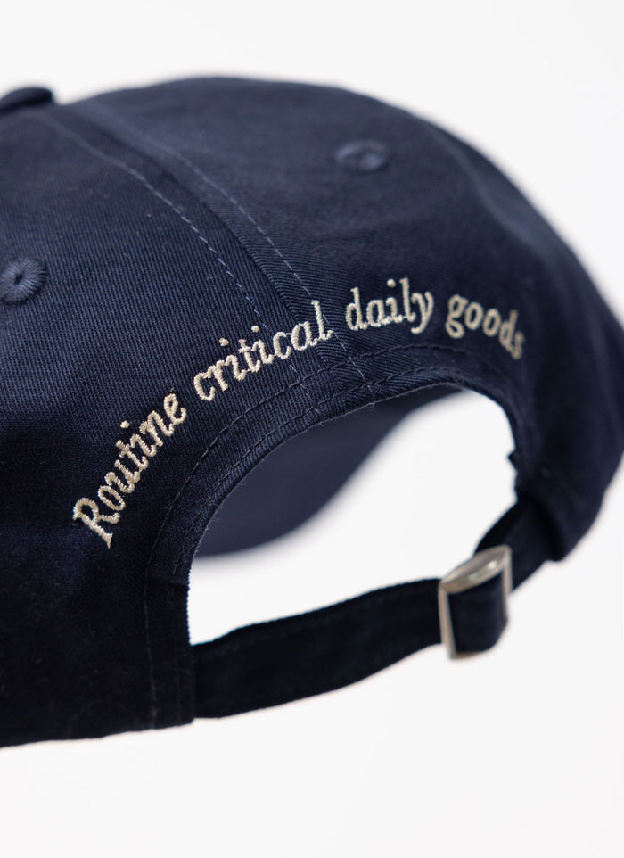 Close-up of the Percival World Key Cap in navy, detailing the 'Routine critical daily goods' embroidery on the back.