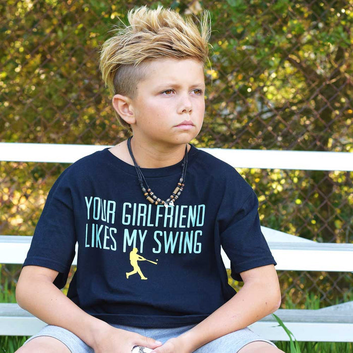 Youth model wearing black youth graphic tee with “Your Girlfriend Likes My Swing” design